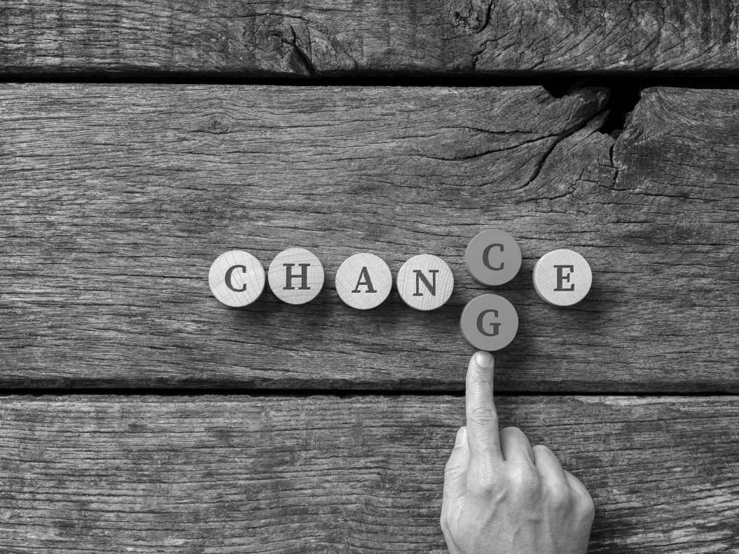 Word Chance spelled on wooden cut circles with male hand pusing in letter G to change it into Change.
